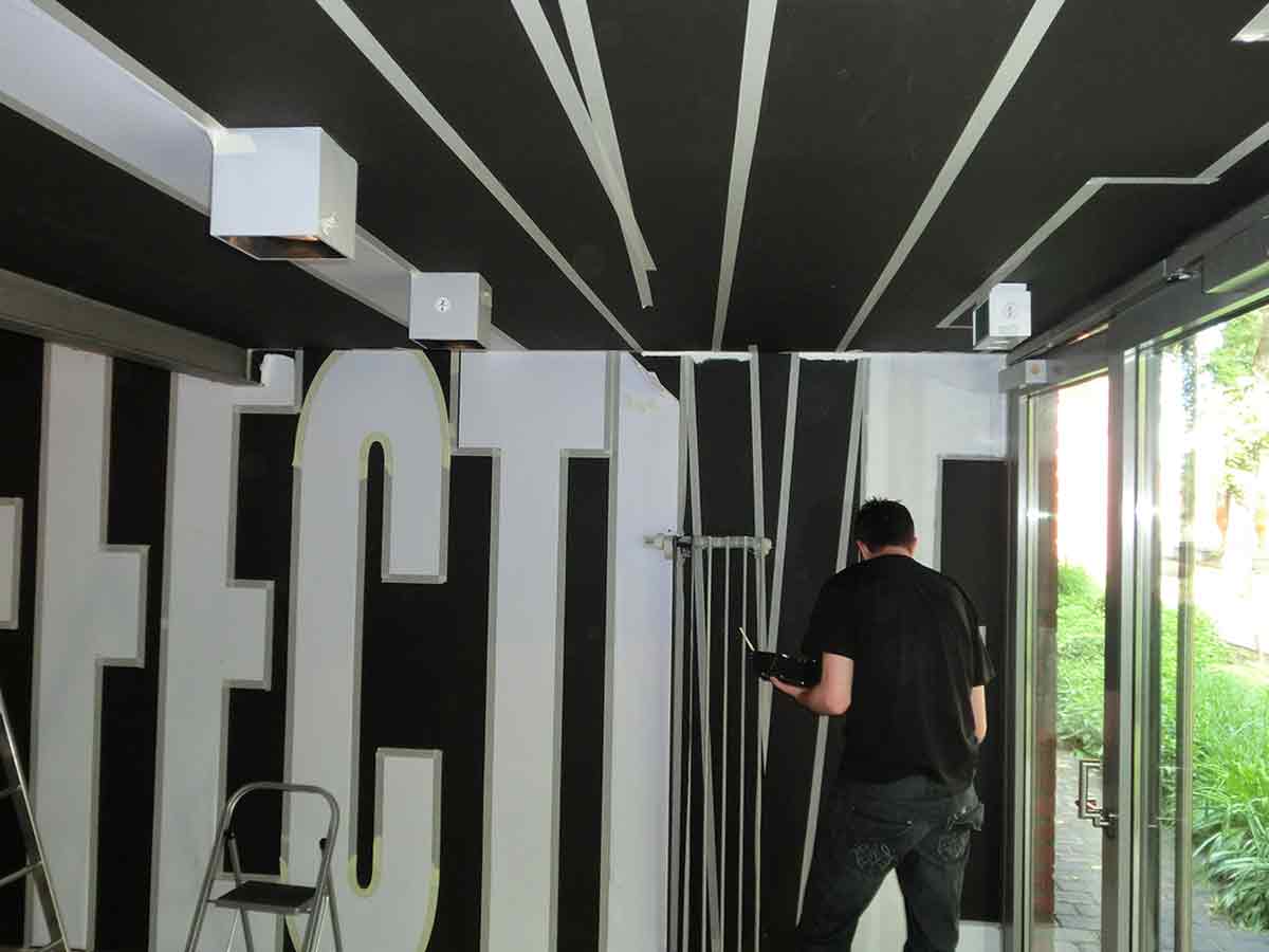 Team trägt mithilfe von Schablonen Wandfarbe auf, um das Vinyl Lettering zu ersetzen